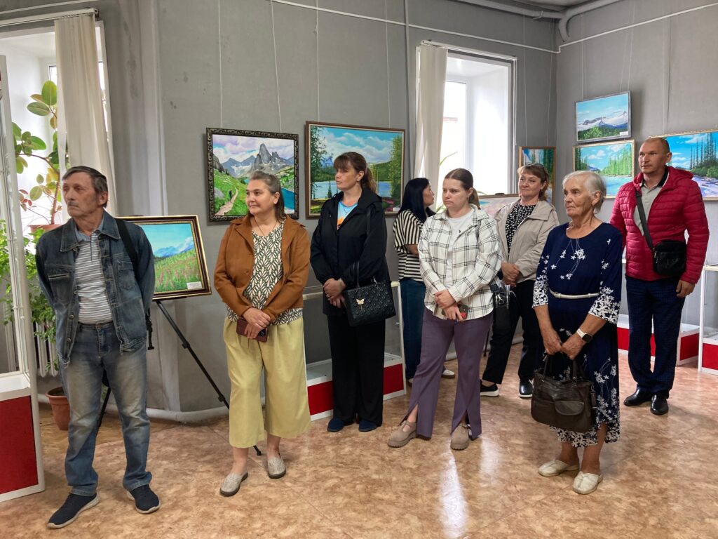 Группа посетителей стоит в светлом зале художественной выставки картин